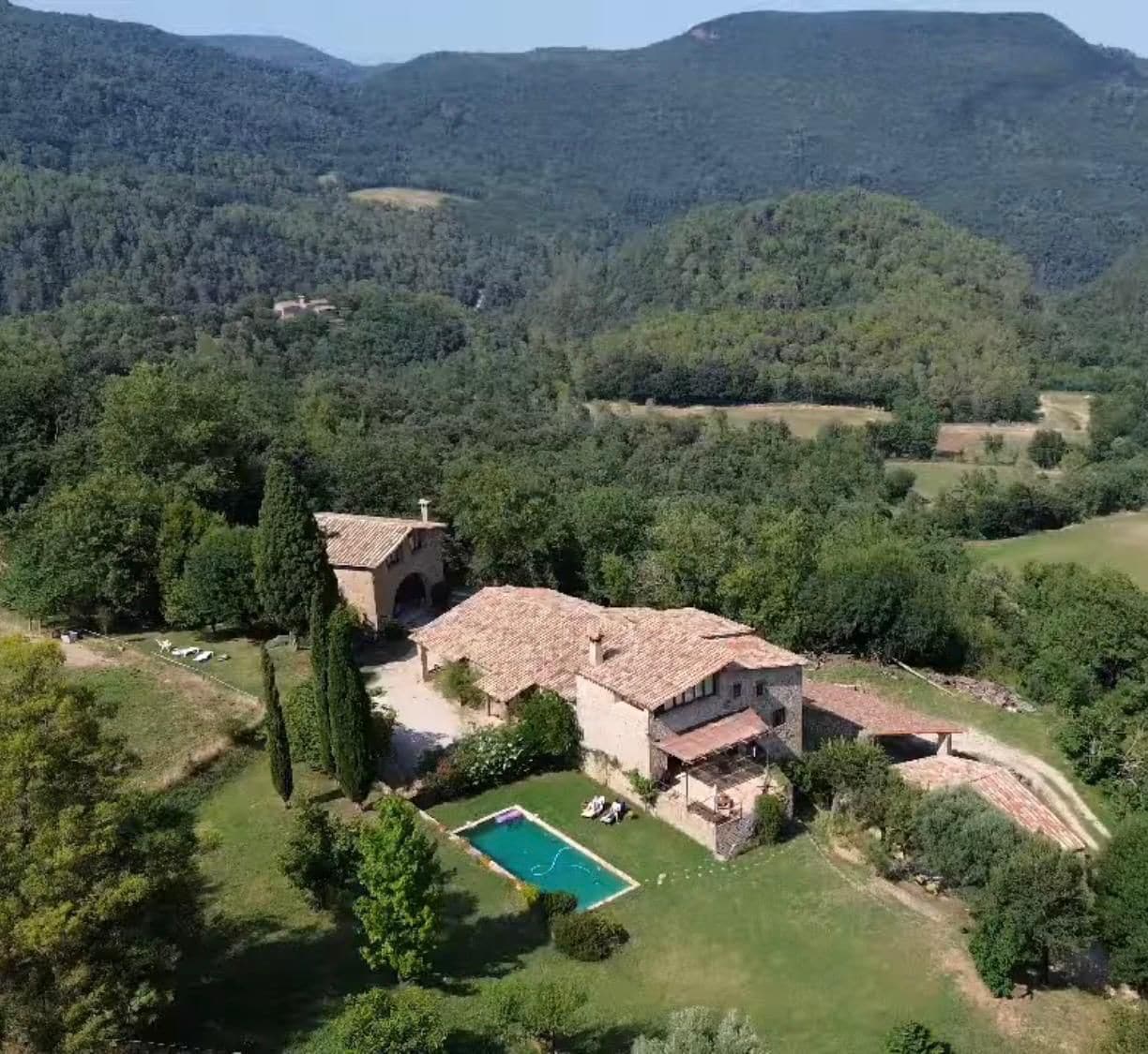 A villa with a swimming pool, surrounded by lush greenery and hills.