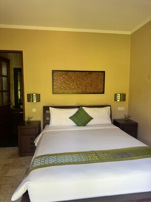 A hotel room with a bed, a wall-mounted artwork, bedside lamps, and a nightstand with a plant. - Charming 1-bedroom apartment with AC and pool (Gianyar)