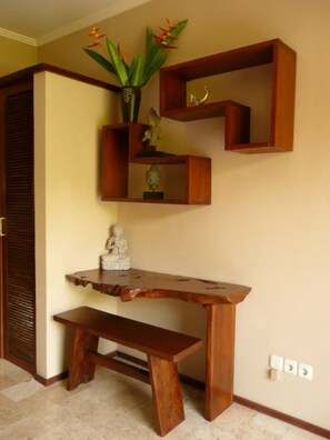 A wooden desk with a bench, a Buddha statue, and a plant with red flowers. - Charming 1-bedroom apartment with AC and pool (Gianyar)
