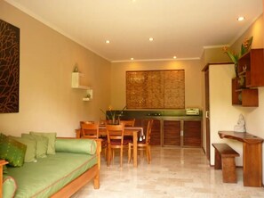 A living room with a sofa, dining table, chairs, and a kitchen area with cabinets and a countertop. - Charming 1-bedroom apartment with AC and pool (Gianyar)