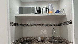 Een kleine keuken met een magnetron, koffiezetapparaat en blender op het aanrecht, een spoelbak en een vaatwasser eronder.