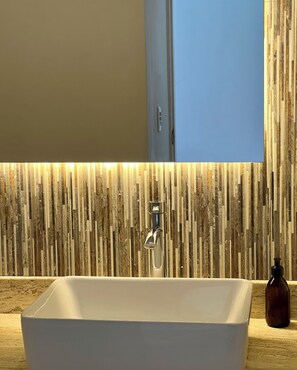 Ein Badezimmer mit einem weißen Waschbecken, einem Spiegel und einer Wand mit Holzstruktur.