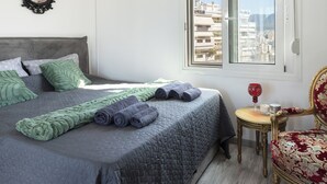 A neatly made bed with rolled towels, a small table with a glass, and a chair with a patterned cushion. - Kristy's 360 view elegant rooftop flat (Zografou)