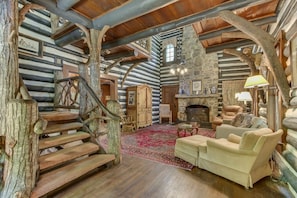 A log cabin interior with a fireplace, a staircase, and a cozy seating area.