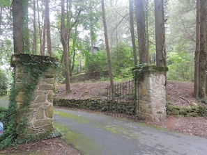 A stone archway leading into a forested area with a paved path.