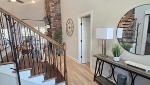 A staircase with wooden steps and black railings, a round mirror, a lamp, and a potted plant on a console table. - Lake Days & Nashville Nights — Private Dock, Game Room & Fire Pit - Room for 12 (Gallatin)