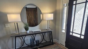 A hallway with a wooden console table, two wall-mounted lamps, a mirror, and a potted plant. - Lake Days & Nashville Nights — Private Dock, Game Room & Fire Pit - Room for 12 (Gallatin)