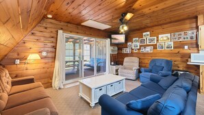 A cozy room with a wooden ceiling, a large window, a sofa, a chair, and a television. - Juniper Presents: Chalet #50 Near Courts & Family Resort Fun (Stevensville)
