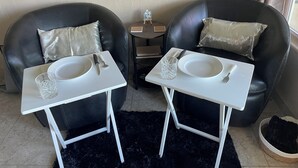 Two black leather chairs with cushions, a small white table with a bowl, plate, knife, and glass, and a black furry rug.