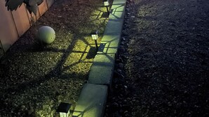 A wooden building with a metal sign, a paved pathway, and a garden with a bird sculpture and a spherical object.