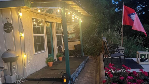 A building with a porch, string lights, a flag, and potted plants.