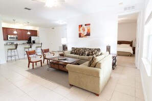 A living room with a sofa, coffee table, and chairs, a kitchen with cabinets and appliances, and a bedroom with a bed and nightstand. - ★5min➡️Universal | Spacious Condo ★ VC101 (Orlando)