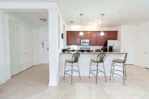 A kitchen with white cabinets, a microwave, a stove, and three bar stools. - ★5min➡️Universal | Spacious Condo ★ VC101 (Orlando)