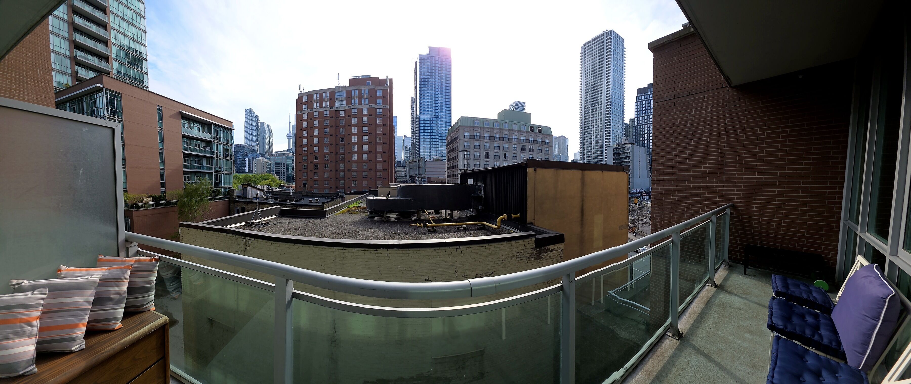 Una terraza en la azotea con vistas a edificios de la ciudad, una barandilla metálica y una peque ña estructura de madera.