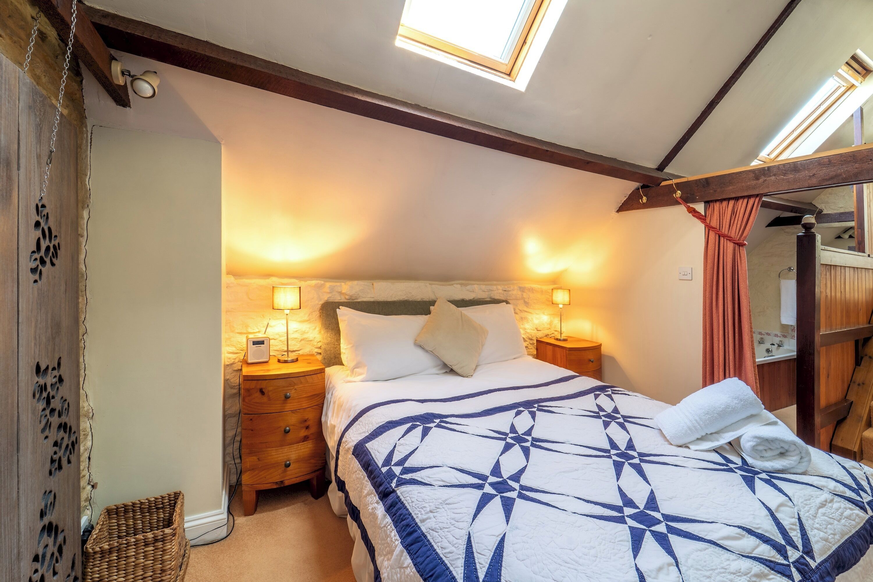 Une chambre à coucher avec un lit, des lampes de chevet, une tête de lit en bois, un petit panier en osier et un puits de lumière.