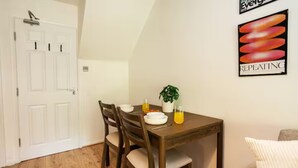 Een eetgedeelte met een houten tafel, vier stoelen, een potplant en een kunstwerk aan de muur.