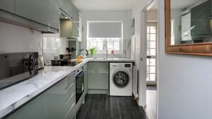 Een kleine keuken met een wasmachine, een spoelbak en een raam.