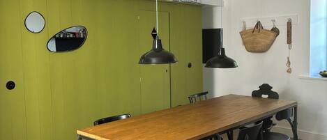 Un comedor con mesa de madera y sillas negras, un muro verde decorativo y una cesta colgante.