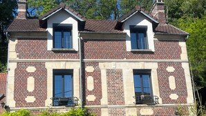 A two-story house with a brick facade, two visible windows, a chimney, and a black metal fence. - Charming house (Béthisy-Saint-Martin)