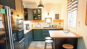A kitchen with dark cabinets, a wooden countertop, a hanging light fixture, and a window with blinds. - Charming house (Béthisy-Saint-Martin)