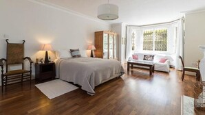 A bedroom with a bed, bedside tables, a window seat, and a wooden floor. - Elegant 2 bed near Hampstead & Camden (London)
