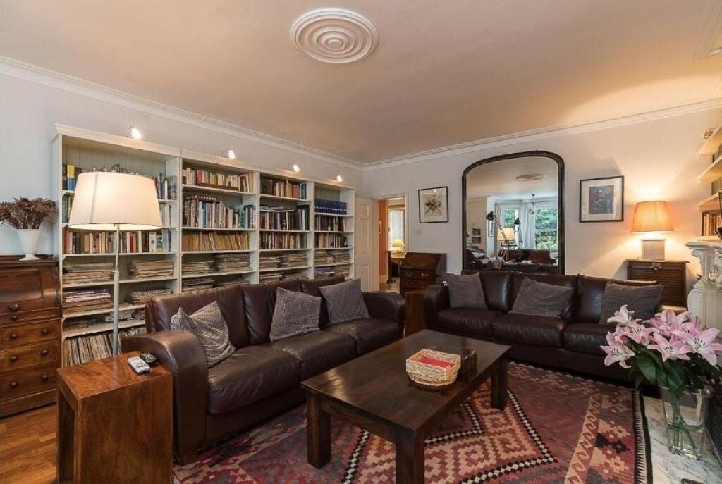 Un salon avec un canapé en cuir marron, une table basse, une bibliothèque et un miroir.