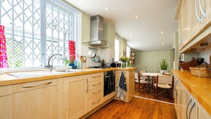 A modern kitchen with wooden cabinets, a central island, and a dining area with a table and chairs. - Elegant 2 bed near Hampstead & Camden (London)