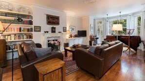 A living room with a fireplace, bookshelves, a sofa, a television, and a piano. - Elegant 2 bed near Hampstead & Camden (London)