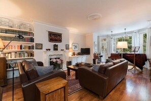 Ein Wohnzimmer mit Kamin, Bücherregalen, einer Couch, einem Fernseher und einem Klavier.