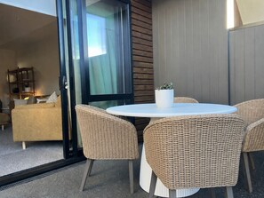 Ein moderner Außenbereich mit Korbstühlen und einem runden Tisch, einer Schiebetür und Blick auf ein Wohnzimmer.