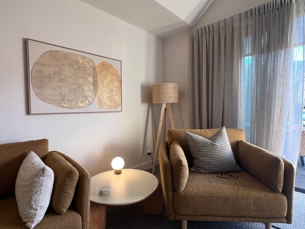 A modern hotel room with a sofa, a small table with a lamp, and a large abstract painting on the wall.