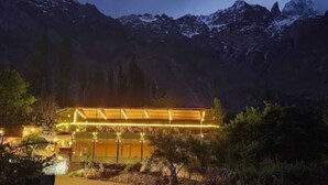 A modern building with a glass facade, surrounded by trees and mountains.