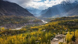 A mountainous landscape with a river, trees, and buildings.
