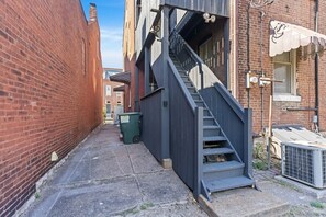 A narrow alley with a brick building, a metal staircase, and a green dumpster.
