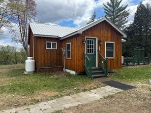 A wooden cabin with a metal roof, a green door, and a small staircase.