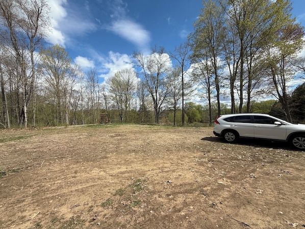 A white car parked in a dry, open field with trees in the background.
