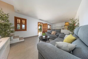 Una sala de estar moderna con un sofá gris, una mesita redonda y una cocina al fondo.