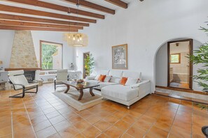 A spacious living room with a fireplace, a sofa set, a dining table, and a large window. - Delightful Countryside Retreat, A/C, Private Pool - 10mins drive from Ancient Towns & Sandy Beaches (Pollença)
