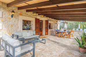 Eine Terrasse mit Steinsäulen, einer Couch, einem Esstisch mit Stühlen und einem Blumentopf.