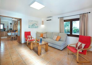 Ein Wohnzimmer mit einer Couch, zwei roten Sesseln, einem Holztisch und einem Essbereich mit Tisch und Stühlen.