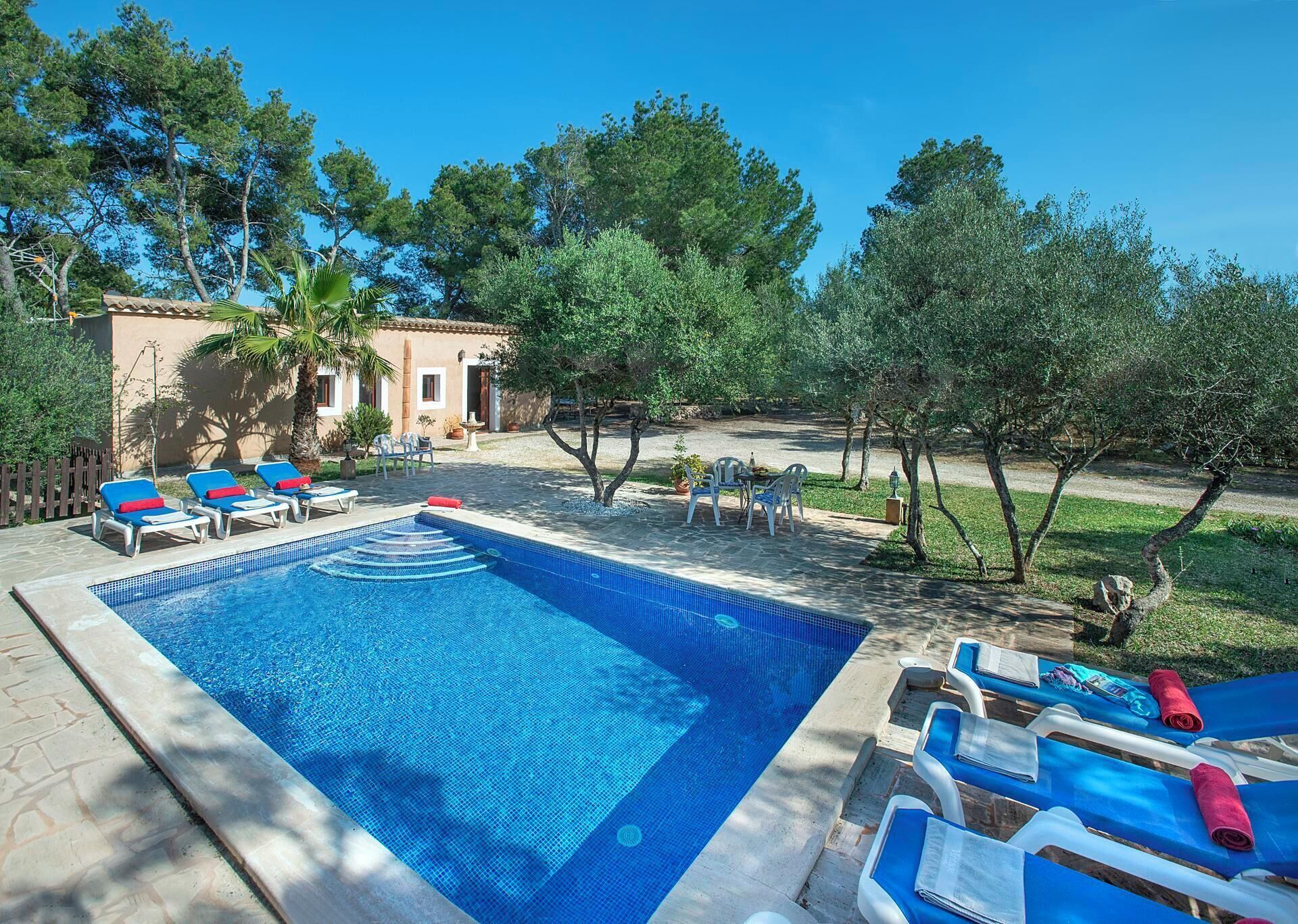 Une piscine avec des chaises longues, un petit bâtiment et des arbres en arrière-plan.