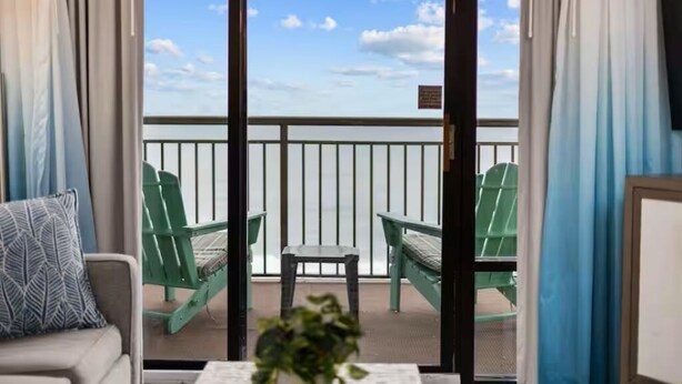 A room with a view of the balcony, green chairs, a small table, and a sofa. - Park at Your Door! Direct Oceanfront + Waterpark (Myrtle Beach)
