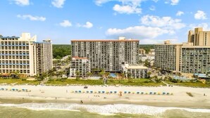 A beachfront hotel with multiple high-rise buildings, a sandy beach, and umbrellas. - Park at Your Door! Direct Oceanfront + Waterpark (Myrtle Beach)