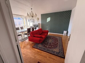 Una sala de estar con un sofá rojo, un tapete estampado, una araña y una pared verde con diseño.