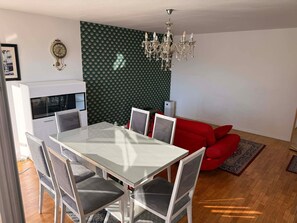 Un comedor con una mesa y sillas blancas, un sofá rojo, una araña y una pared con textura.