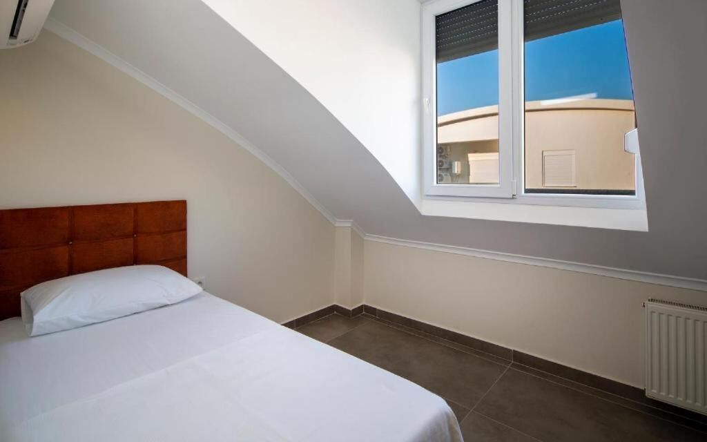 Une chambre avec un plafond en pente, un lit, une fenêtre et un radiateur.
