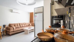Una cocina moderna con estufa, horno y ollas. En la sala de estar hay un sofá y una pequeña mesa.