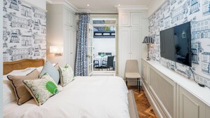 A bedroom with a bed, pillows, a TV, and a view of an outdoor dining area. - Charming 1BR Retreat in Pimlico (London)