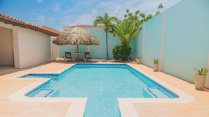 A swimming pool with a tiled deck, a thatched umbrella, and a few chairs. -     Wayaca Oasis Retreat-Private Pool + 4BR + Prime Location in Aruba (Oranjestad)