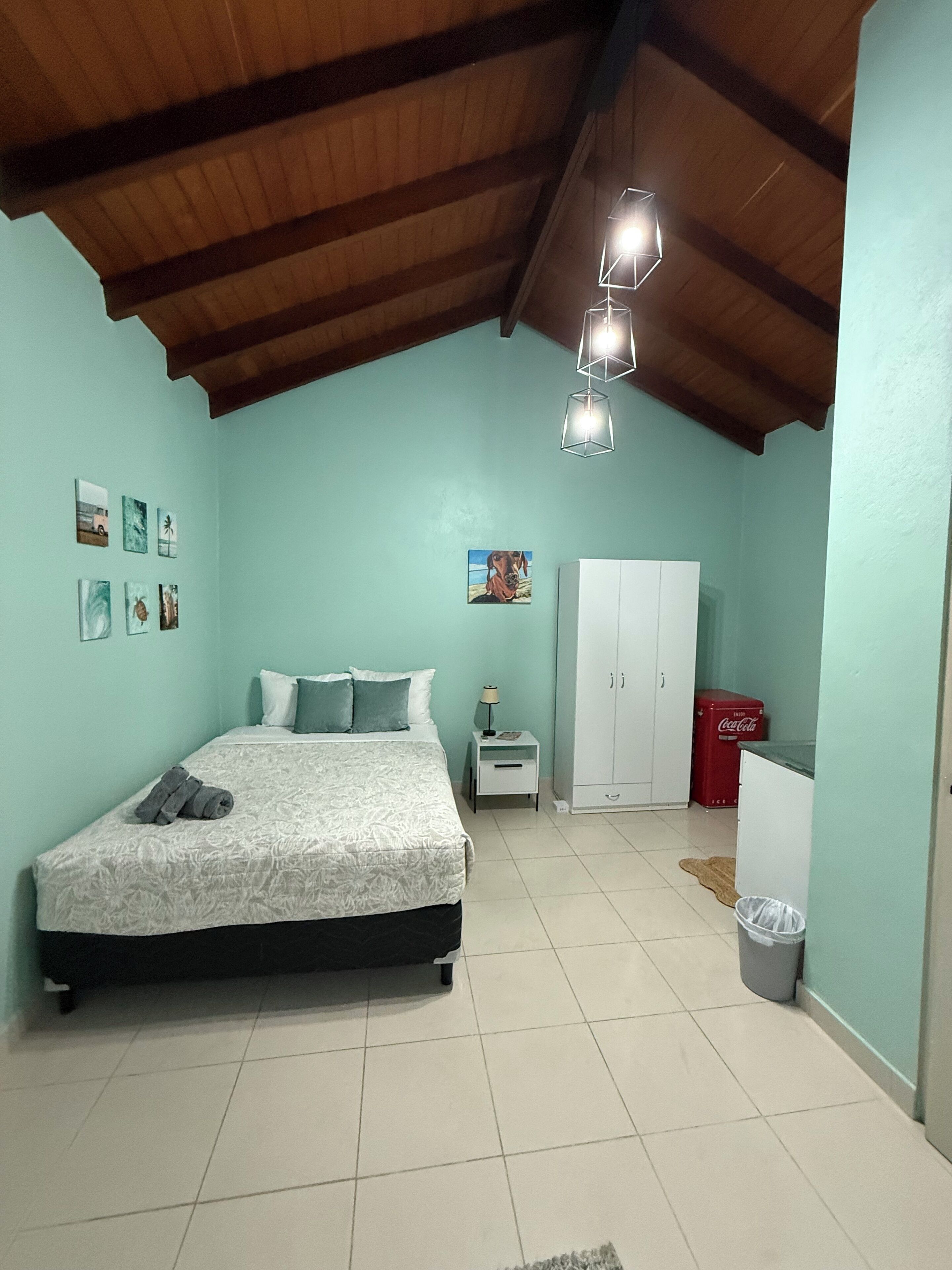 A bedroom with a bed, a nightstand, a wardrobe, and a trash bin.